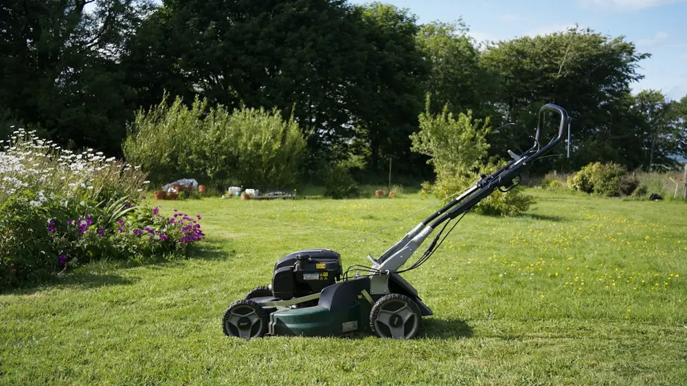 Rasenmäher auf einem gepflegten Rasen vor blühenden Beeten
