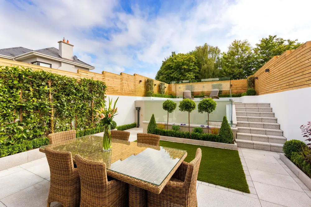 Gepflegter Garten mit Rasen und Pflanzen vor einer sauberen Terrasse mit Glastüren